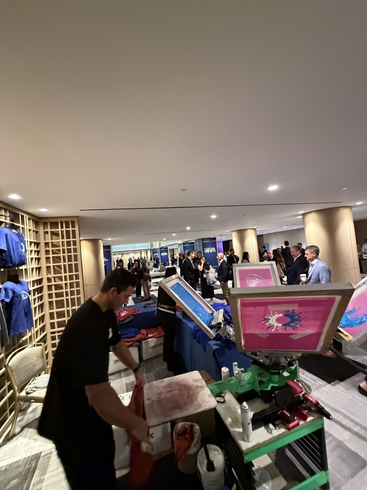 Interior booth setup with printed tote bags and various decorated apparel products displayed at a trade show